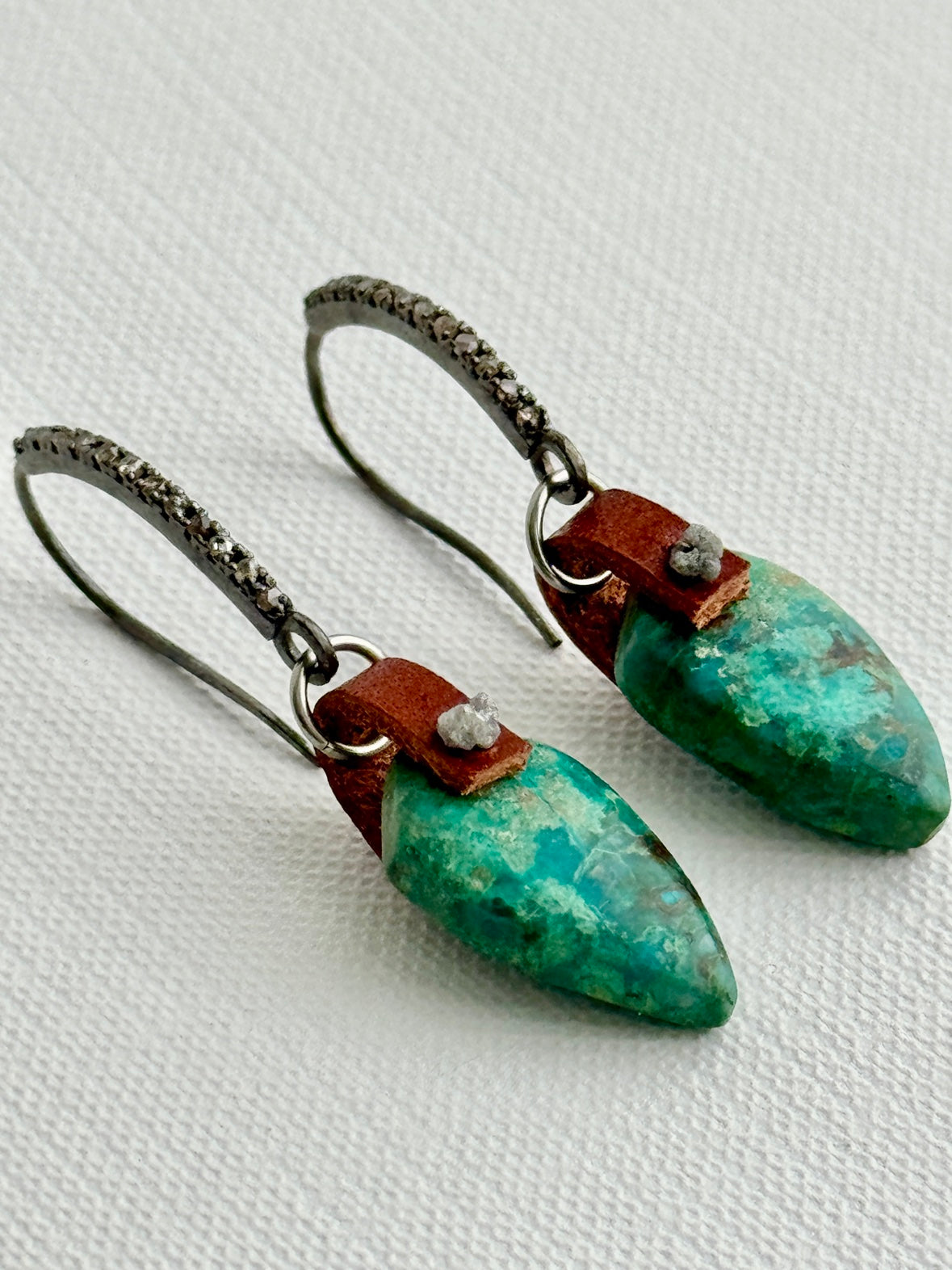 Turquoise chrysocolla shield earrings with raw diamond and oxidized sterling pavé ear hooks, lying close-up