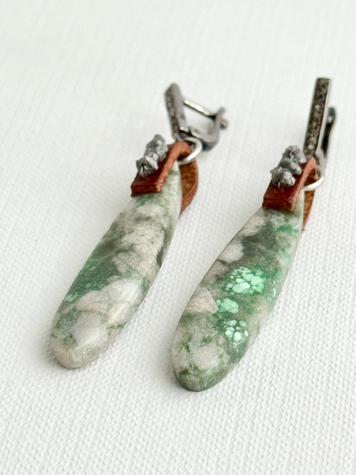 Utah variscite teardrop earrings lying on white fabric, pale sage stones, chestnut leather loops