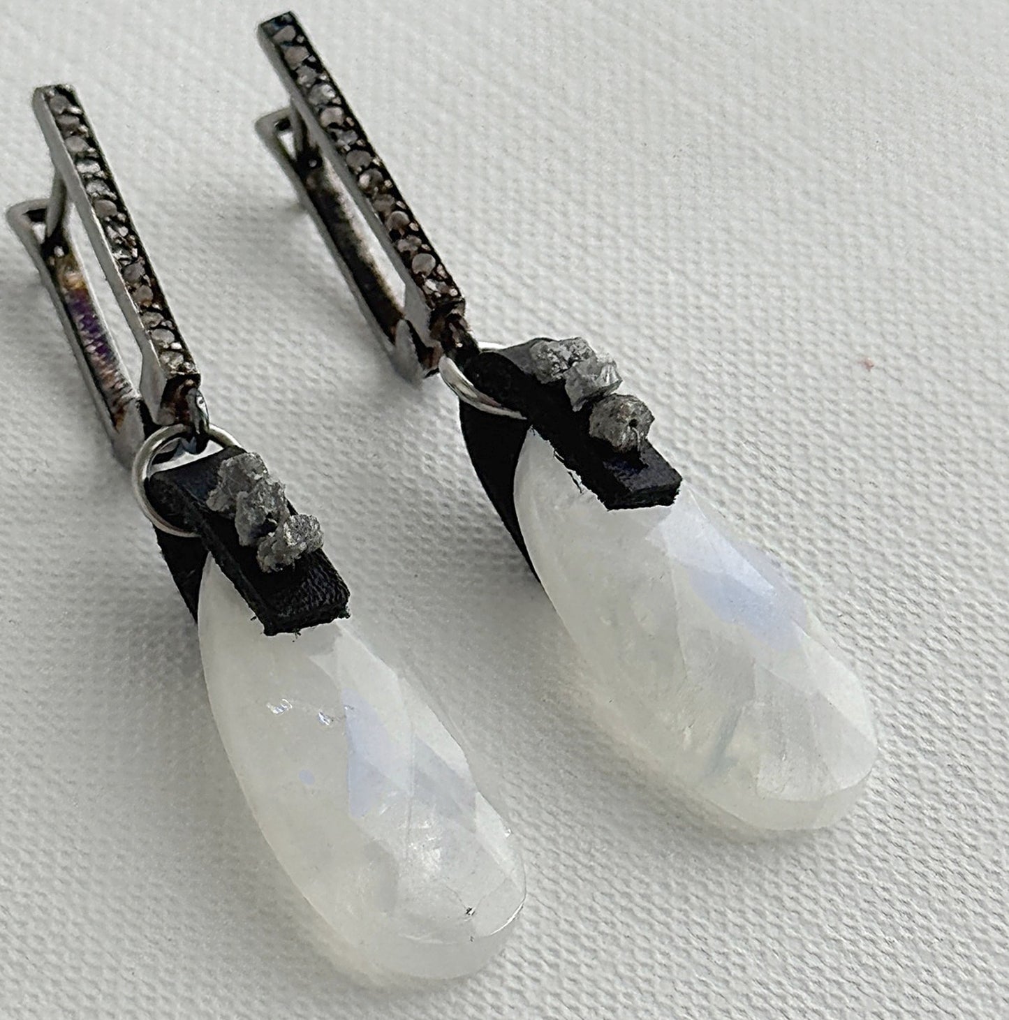 Close-up of rainbow moonstone teardrop earrings with raw grey diamonds on black leather and oxidized sterling silver pavé leverbacks