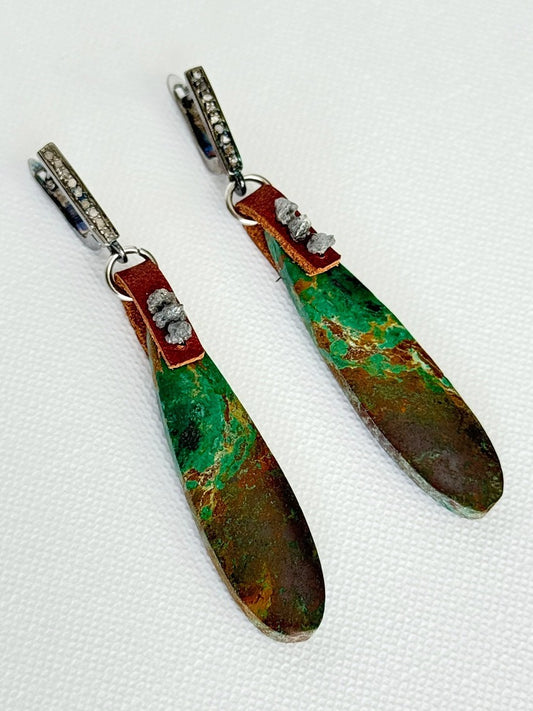 Chrysocolla teardrop earrings angled close, green and copper-brown stones, raw grey diamonds on brown leather