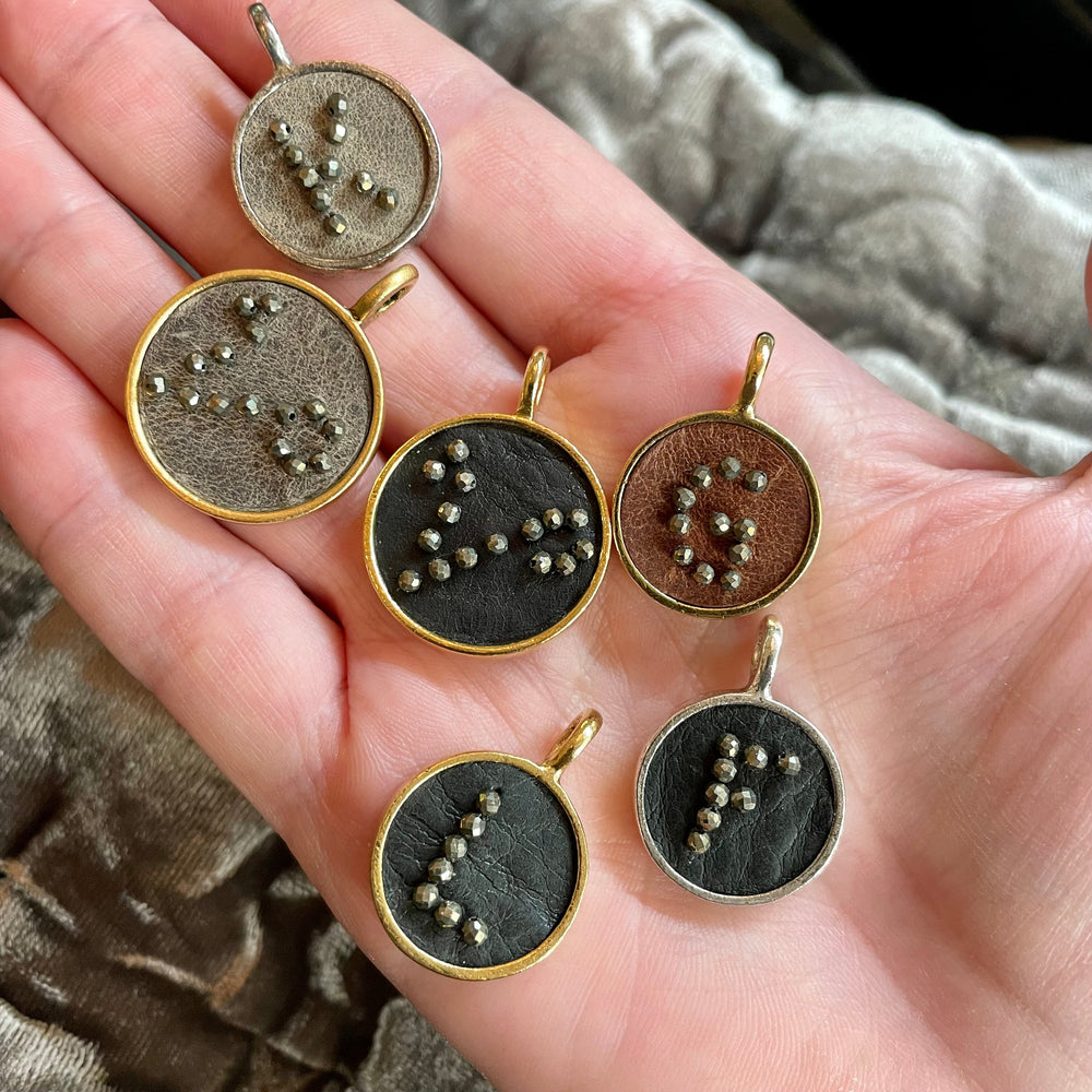 Hand holding initial charms in gold and silver finishes