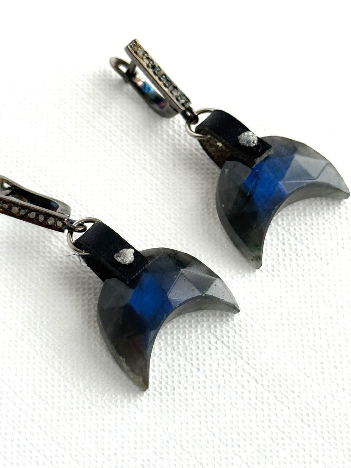 Faceted labradorite crescent earrings flashing blue, with a hand-sewn raw grey diamond on black leather and oxidized sterling pavé diamond leverbacks, angled close-up