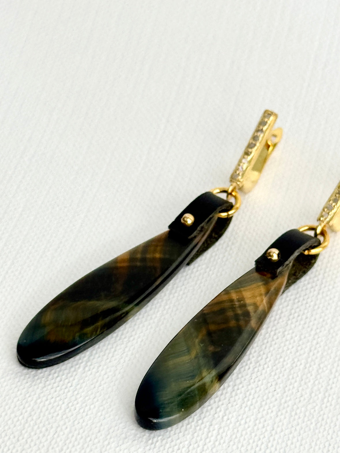 Tiger’s eye teardrop earrings lying angled, plaid-patterned stones, black leather, gold bead