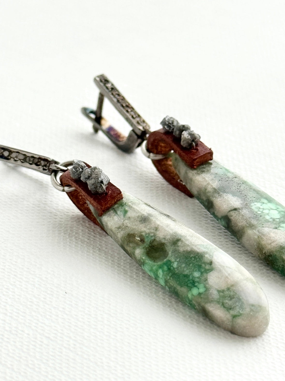 Utah variscite teardrop earrings lying angled, sage green stones, chestnut leather, raw grey diamonds