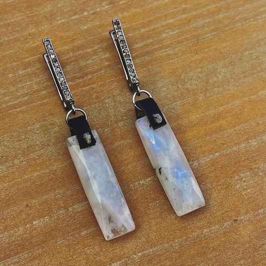 Faceted rainbow moonstone rectangle earrings showing the blue flash, with raw grey diamonds on black leather and pavé-set diamond leverbacks in sterling silver